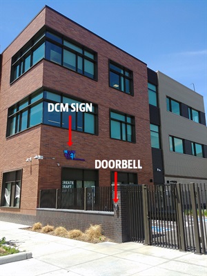 Photo of courtyard entrance, highlighting DCM signage on building and doorbell on exterior fence