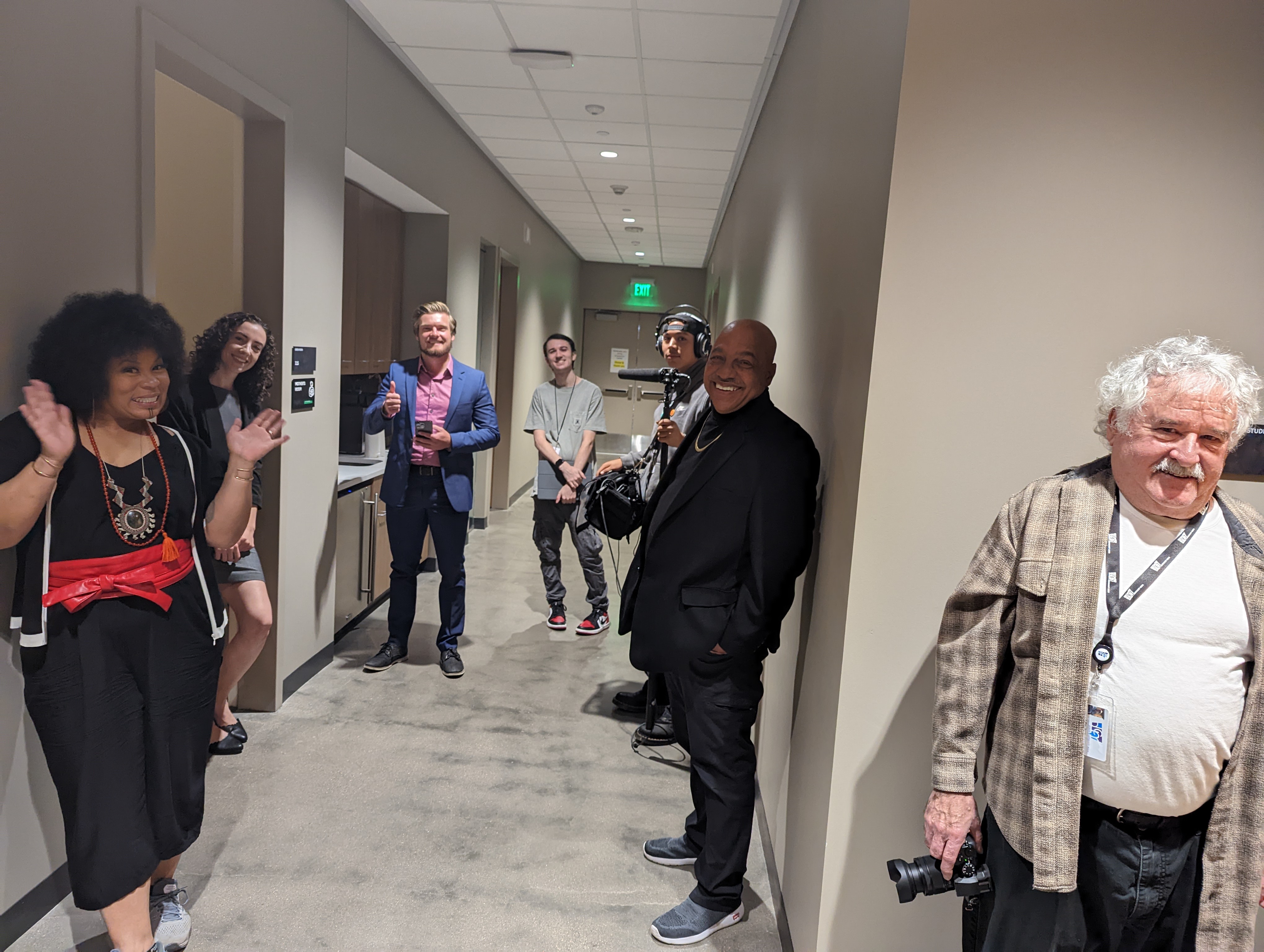 7 members of a production crew standing in a hallway waving