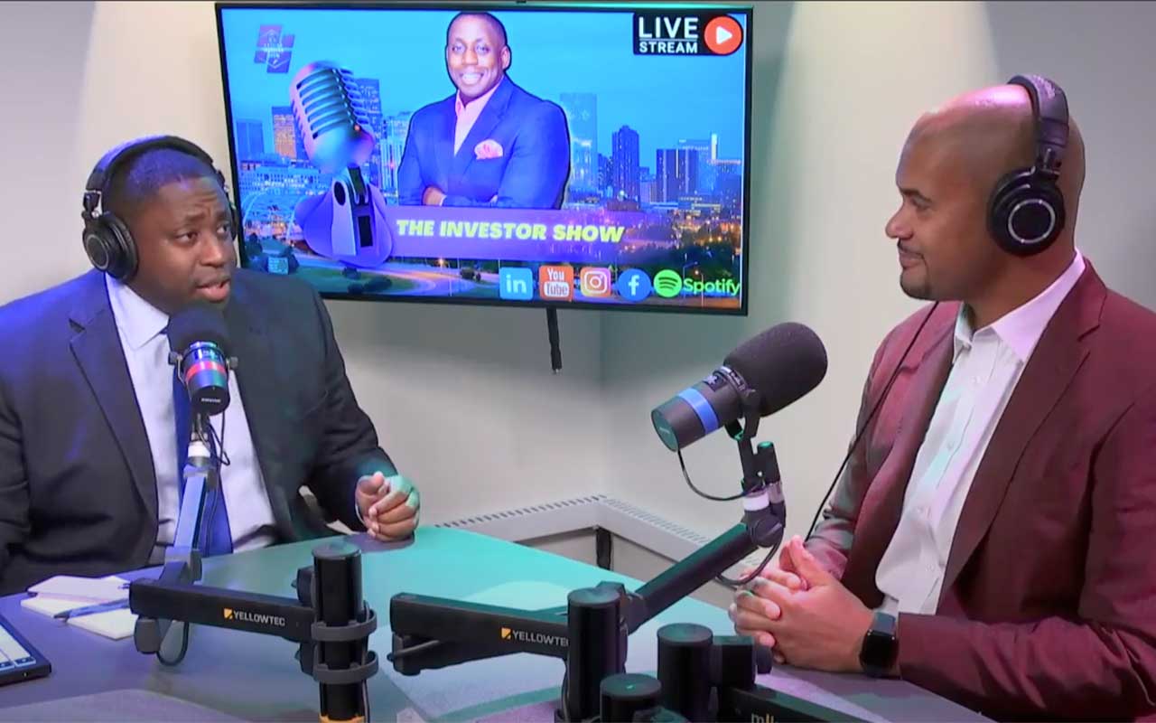 two podcasters at a table with a screen behind them